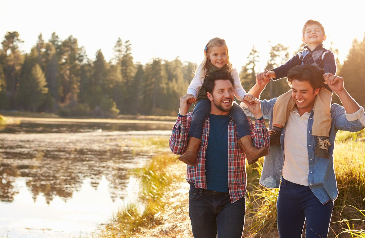 Two men from the LGBTQ+ community with their children walking in a park.