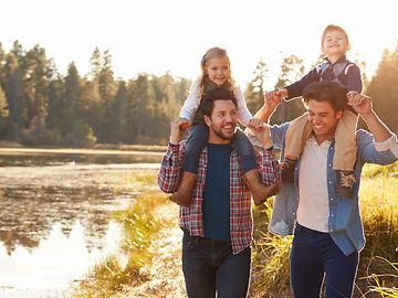 Two men from the LGBTQ+ community with their children walking in a park.