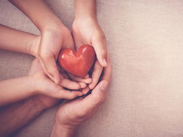 Several pairs of hands holding a heart.