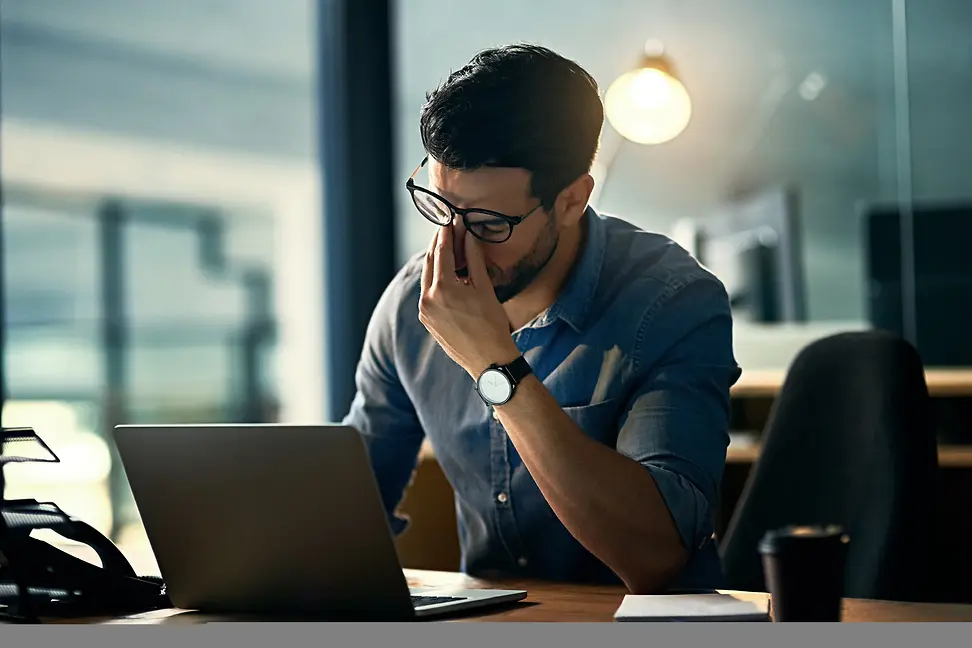 Tired man rubs his eyes during work