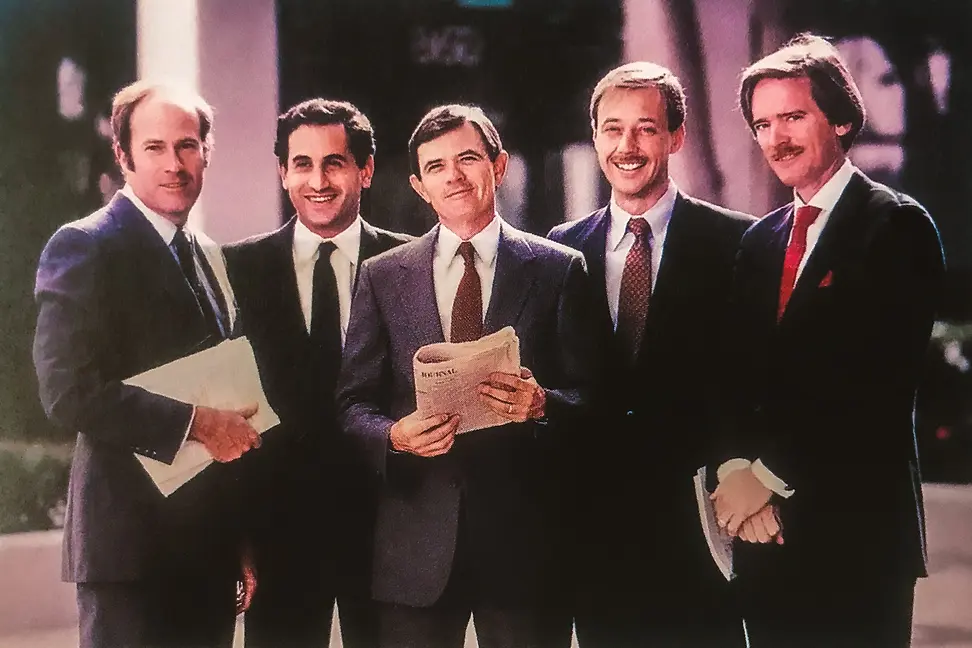 Five men in suits holding documents stand in front of a building; the image has a historical quality.
