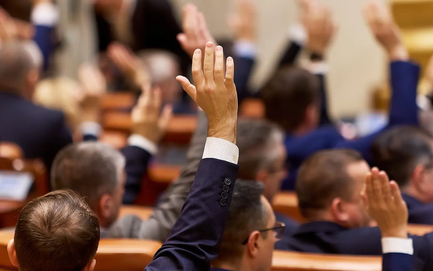 male with hand raised in voting session.